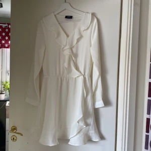 Vit volangklänning från Object - Superfin vit kortklänning från Object med långa ärmar och v-ringning. Klänningen har volangdetaljer längs halsringningen och nertill, samt markerad midja.🌸Finns ingen storlek kvar på klänningen men skulle uppskatta den till ungefär M