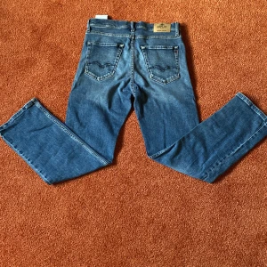 Replay thad - Snygga blå jeans från Replay med klassisk femficksdesign och raka ben. Jeansen har en mellanblå tvätt med lätt slitning och detaljerade bakfickor. Perfekta för en avslappnad och cool stil.