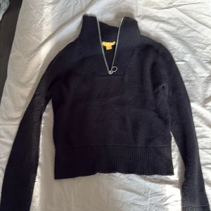 Svart ribbad stickad tröja Gina Tricot - Svart ribbstickad tröja från Gina Tricot med hög krage och snygg silverfärgad dragkedja framtill. Tröjan har lång ärm och croppad passform, perfekt till jeans eller kjol. Materialet är mjukt och värmande, och dragkedjan har en cool ringdetalj.