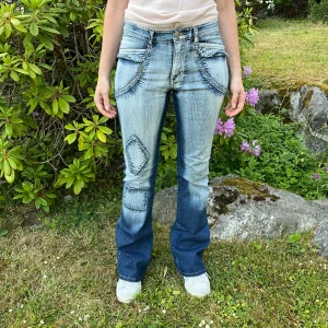 Unika bootcut jeans - Säljer ett par riktigt coola bootcut jeans i ljusblå och mörkblå denim med slitningar, patchdetalj på benet och markerade fickor fram och bak. 🩷 Midja: 37 cm 🩷 Ytterben: 103 cm 🩷 Innerben: 80cm 🩷