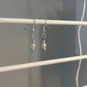 Silvriga örhängen med pärldetalj - Snygga hängande örhängen i silverfärg med små runda pärlor och metallkulor. De har en enkel och stilren design som passar perfekt till din vardagsstil eller när du vill addera något extra till din look. De är egen gjorda!