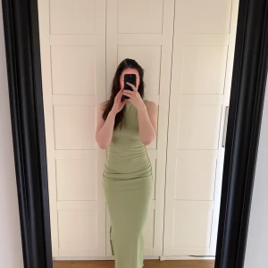 Ljusgrön ärmlös långklänning - Säljer en snygg ljusgrön långklänning med tight passform och ärmlös design. Klänningen har högt skuren hals och smickrande rynkade detaljer vid midjan. Perfekt för dig som gillar stilrena och trendiga plagg.