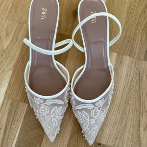 Beige spetsiga pumps med broderi från Zara - Superfina pumps från Zara i beige med spetsig tå och låg klack. Skorna har tunna remmar och är täckta av broderade blommor och pärldetaljer för en riktigt elegant look. Perfekta för dig som vill sticka ut med en romantisk och trendig stil. har faktisk storlek 38 men de passar perfekt. Jag hade på mig dem bara en gång 