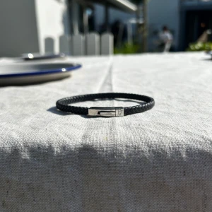 Svart flätat armband från Efva Attling - Snyggt svart armband i flätat läder från Efva Attling med stilren magnetlås i silverfärgad metall. Perfekt accessoar för en clean och modern look. Låset har Efva Attlings logga ingraverad för extra detalj.