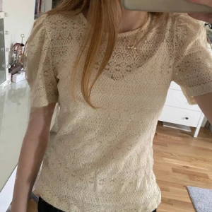 Beige spetsblus med kort ärm - Säljer en beige blus i spets med korta ärmar och rund halsringning. Perfekt att styla med jeans eller kjol för en trendig look. Knappt använd🥰🥰