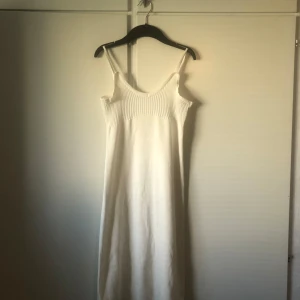 Vit långklänning med slits - Säljer en stilren vit långklänning med smala axelband och ribbad detalj upptill. Klänningen har en snygg slits på sidan och är gjord i ett mjukt, stickat material. Perfekt för varma dagar när du vill känna dig både chill och snygg.