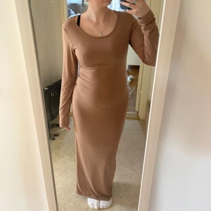 Beige brun långärmad maxiklänning - Säljer en beige långklänning med lång ärm och rundad halsringning. Klänningen är figurnära och har en enkel, stilren design som passar perfekt för dig som gillar minimalistiskt mode. Materialet känns mjukt och följsamt mot kroppen. Och tyget är tunt och luftigt uppskattat storlek Xs 