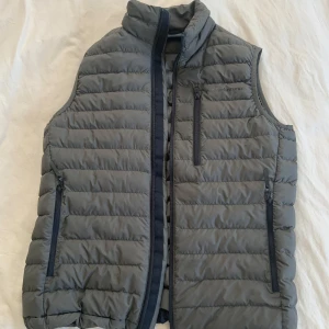  Mörk grön dunväst från Peak Performance - Snygg mörk grön dunväst från Peak Performance med dragkedja och praktiska fickor. Perfekt för kyliga dagar och ger en sportig look. Västen har en stilren design med diskret logga på bröstet. Nypris 2200 kr