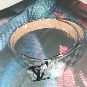 Rutig bälte med monogramspänne - Snyggt rutig bälte med ett iögonfallande monogramspänne. Bältet har en klassisk design med en modern twist, perfekt för att lyfta vilken outfit som helst. Det är gjort i ett stilrent material som ger en lyxig känsla.