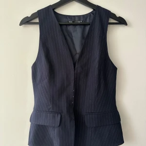 Mörkblå randig väst från Zara - Snygg mörkblå väst från Zara med diskreta ränder. Västen har en v-ringad design och knäppning framtill. Perfekt för en stilren look.