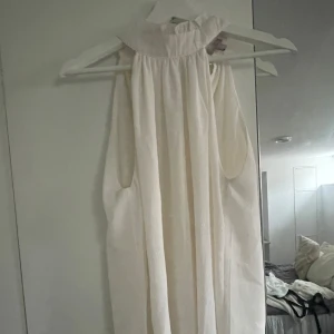 snygg vit blus! - Säljer en assnygg vit blus med hög krage och ärmlös design. Perfekt för sommarens varma dagar. Klänningen har en luftig passform och är tillverkad i ett lätt material som ger en skön känsla. Passar utmärkt för både avslappnade och mer formella tillfällen.