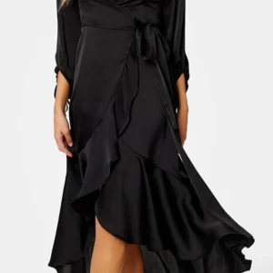 Svart omlottklänning med knytband - Elegant svart omlottklänning i satin med knytband i midjan och volangdetaljer. Klänningen har trekvartsärmar och en v-ringad halslinje, perfekt för festliga tillfällen.