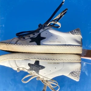 Vita sneakers med stjärndetalj - Snygga vita sneakers med en svart stjärna på sidan och glittriga detaljer vid hälen. Skorna har snörning med text och en klassisk design som passar perfekt för en avslappnad stil. Storlek 38-39