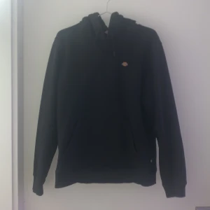 Svart hoodie från Dickies - Säljer en klassisk svart hoodie från Dickies i storlek XS. Tröjan har en justerbar huva och en liten logotyp på bröstet. Perfekt för en avslappnad stil. 🖤Ena snöret saknar plastbiten, annars nyskick. Den är köpt för ca 800kr men säljer för 300kr