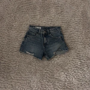 Jeansshorts från Zara - Snygga jeansshorts från Zara i en klassisk blå färg. De har  fransiga kanter och slitna detaljer för en trendig look. Perfekta för sommarens alla äventyr!