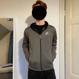 Grå/ grön hoodie från Nike - Säljer en grå/grön hoodie från Nike med dragkedja och vit loga på bröstet. Hoodien har svarta detaljer längs ärmarna. Perfekt för en sportig look! Det finns fläckar på hoodien syns på bilderna avgör själv.