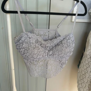 Blått spetslinne - Säljer en söt vit spetslinne med smala axelband och blommigt mönster. Toppen är croppad och perfekt till våren och sommaren