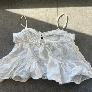 Vit ärmlös blus med spetsdetaljer från Zara - Söt vit blus med tunna axelband och spetsdetaljer. Blusen har en luftig passform och knytning framtill. Perfekt för varma sommardagar. Stl M men passar även en small
