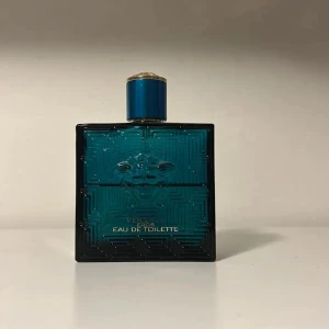 Versace Eros Eau de Toilette - Säljer en elegant Versace Eros Eau de Toilette i en stilren blå glasflaska med ett klassiskt grekiskt mönster och Versace-logotypen. Flaskan har en fyrkantig form och en matchande blå kork med gulddetaljer. Perfekt för den som vill ha en fräsch och maskulin doft. Jag säljer för att jag behöver pengarna. Det är ungefär 50 ml kvar i flaskan. MVH Leo