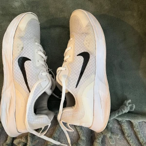 Vita Nike sneakers med svart logga - Säljer ett par vita Nike sneakers med svart logga. Skorna har en stilren design med snörning och en bekväm passform. Perfekta för både träning och vardag.