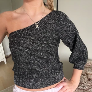 Glittrig oneshoulder topp - Säljer en snygg glittrig oneshoulder topp i svart och silver. Toppen har en tight passform och trekvartsärm, perfekt för en kväll ute. Den är croppad och ger en trendig look. Passar bra till både jeans och kjol.
