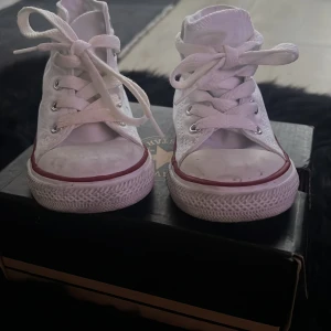 Vita Converse All Star sneakers - Säljer ett par klassiska vita Converse All Star sneakers med snörning. Skorna har en röd rand runt sulan och den ikoniska loggan på sidan. Perfekta för en avslappnad stil.