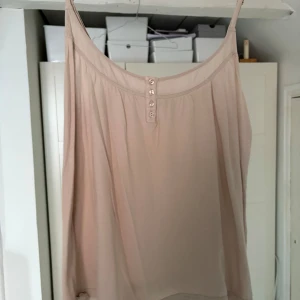 Beige/rosa  linne från Hunkydory - Säljer en stilren beige/rosa linnetopp från Hunkydory. Toppen har smala axelband och dekorativa knappar framtill. Perfekt för varma dagar eller som ett lager under en kavaj.