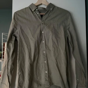 Beige skjorta från GANT - Säljer en stilren beige skjorta från GANT. Skjortan har långa ärmar och knappar framtill. Perfekt för en klassisk look.
