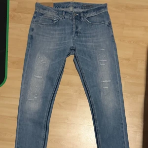 Dondups med slitningar - Snygga blå jeans med slitningar på framsidan och klassisk femficksdesign. De har en knappgylf och är tillverkade i ett bekvämt denimtyg. Perfekta för en avslappnad stil. Skick 7/10 pågrund av några små defekter 