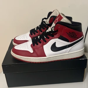 Nike Air Jordans i rött, vitt och svart - Snygga Nike Air Jordans i klassisk röd, vit och svart färgkombination. Skorna har en ikonisk design med snörning och den välkända Nike-loggan på sidan. Perfekta för dig som vill ha en stilren och sportig look.