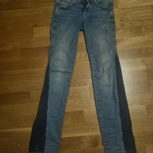 Blå jeans med slitna detaljer - Snygga blå jeans med en tight passform och slitna detaljer för en trendig look. Perfekta för en avslappnad stil. De har en klassisk femficksdesign och dragkedja.