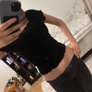 Svart ribbad topp - Säljer en svart ribbad topp med korta ärmar och volangdetaljer vid ärmslut och nederkant. Toppen har en tight passform och är perfekt för en stilren look.💕