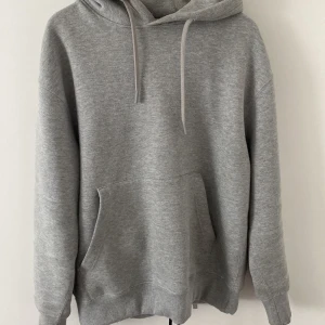 Grå hoodie från Pull&Bear - Säljer en stilren grå hoodie från Pull&Bear. Den har en klassisk design med en stor ficka framtill och justerbar huva. Perfekt för en avslappnad look.