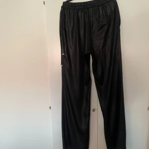 Svarta byxor från Acne Studios - Snygga svarta byxor från Acne Studios i ett glansigt material. Byxorna har en elastisk midja och en avslappnad passform. Perfekta för en stilren look. Byxorna är i riktigt fint skick, använda en gång. Rökfritt hem. Skickar paket som spårbart. 