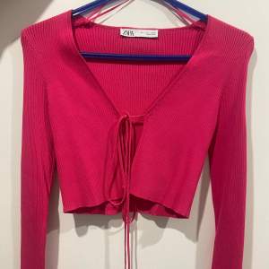 Säljer en snygg rosa ribbad topp från Zara med v-ringning och knytning framtill. Toppen är croppad och har långa ärmar, perfekt för en trendig look. Passar bra till både jeans och kjol. Helt oanvänd!