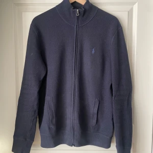 Mörkblå tröja med dragkedja från Polo Ralph Lauren - Säljer en stilren mörkblå tröja från Polo Ralph Lauren. Tröjan har en dragkedja framtill och långa ärmar. Perfekt för en avslappnad och snygg look.