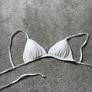 Vit bikiniöverdel - Snygg vit bikiniöverdel med ribbad textur och knytband. Perfekt för sommarens stranddagar. Triangelformad design som ger en klassisk look. Aldrig använd förståss
