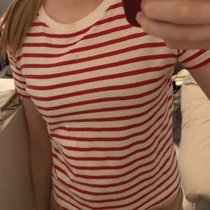 Röd- och vitrandig t-shirt - Säljer en röd- och vitrandig t-shirt med korta ärmar. T-shirten har en rund halsringning och är gjord i ett mjukt material.