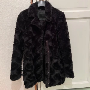 Svart pälsjacka från Vero Moda - Säljer en snygg svart pälsjacka från Vero Moda. Jackan har en klassisk krage och stängs med knappar. Perfekt för att hålla sig varm och stilren under kyliga dagar. Älskar denna kappa, tyvärr har den blivit för liten för mig. Passar perfekt till alla tillfällen. 