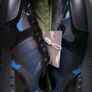 Valentino Rockrunners - Snygga Valentino Rockrunner sneakers i en cool svart och blå camouflage-design. Skorna har snörning och är tillverkade i en kombination av skinn och mocka. Perfekta för att ge din outfit en unik touch.