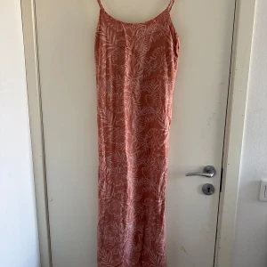 Rosa långklänning  - Säljer en rosa långklänning från Angelology med ett subtilt mönster av vita blad. Klänningen har smala axelband och en avslappnad passform, (katt och kanin finns i hemmet) 