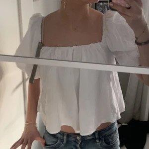 Vit blus med puffärmar och rosett - Säljer en söt vit blus med puffiga kortärmar och en stor rosett i ryggen. Blusen har en luftig passform och en fyrkantig urringning. Perfekt för en somrig look! Den är aldrig använd!💞💞