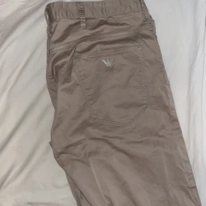 Beige byxor från Emporio Armani - Snygga beige tuna byxor från Emporio Armani med dragkedja och knapp framtill. Byxorna har en stilren design med en diskret logga på bakfickan. Perfekta för sommaren. Fick dom i present men va tyvärr fel storlek 
