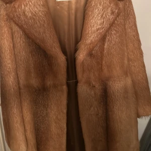 Brun pälsjacka - Säljer en elegant brun pälsjacka med lång längd och klassisk design. Jackan har långa ärmar och en mjuk insida för extra komfort. Perfekt för att hålla sig varm och stilren under kyliga dagar.