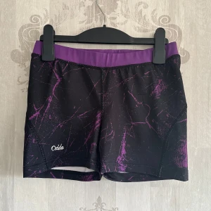 Svarta och lila träningsshorts från Oxide - Snygga träningsshorts från Oxide i svart med lila detaljer och ett abstrakt mönster. Perfekta för gymmet eller löprundan. De har en elastisk midja för extra komfort.