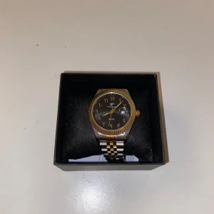 Klassisk herrklocka med tvåfärgad länk - Snygg herrklocka från Omax med en elegant svart urtavla och guldiga detaljer. Klockan har en tvåfärgad länk i silver och guld samt en datumvisare. Perfekt för den som gillar en tidlös stil.