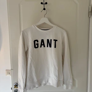 Vit sweatshirt från GANT - Säljer en vit sweatshirt från GANT med svart text på bröstet. Tröjan har långa ärmar och en rund halsringning. Storlek: 158/164.