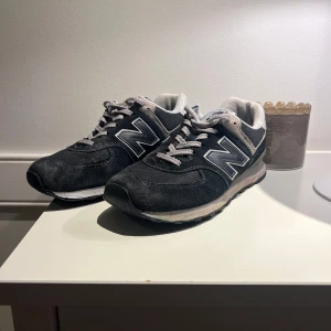 new balance 574 - Tjena, säljer mina 574 då de ej används längre. Det är ett par klassiska mörklbå New Balance sneakers med vita och gråa detaljer. Skorna har en bekväm sula och är perfekta för vardagsbruk. 