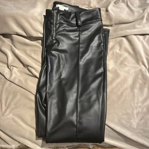 Svarta skinnbyxor från Gina Tricot - Snygga svarta skinnbyxor från Gina Tricot med dragkedja framtill. Byxorna har en stilren design med bälteshällor och en tight passform. Perfekta för en trendig look. (Passar mig som är 167)