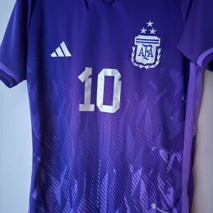 En lila Argentina tröja med Messi 10 på ryggen - Säljer en Argentina fotbollströja från Adidas i lila med nummer 10 och Messi på ryggen. Tröjan har korta ärmar och är tillverkad i lätt och ventilerande polyester, perfekt för match eller träning. Passar både S och M